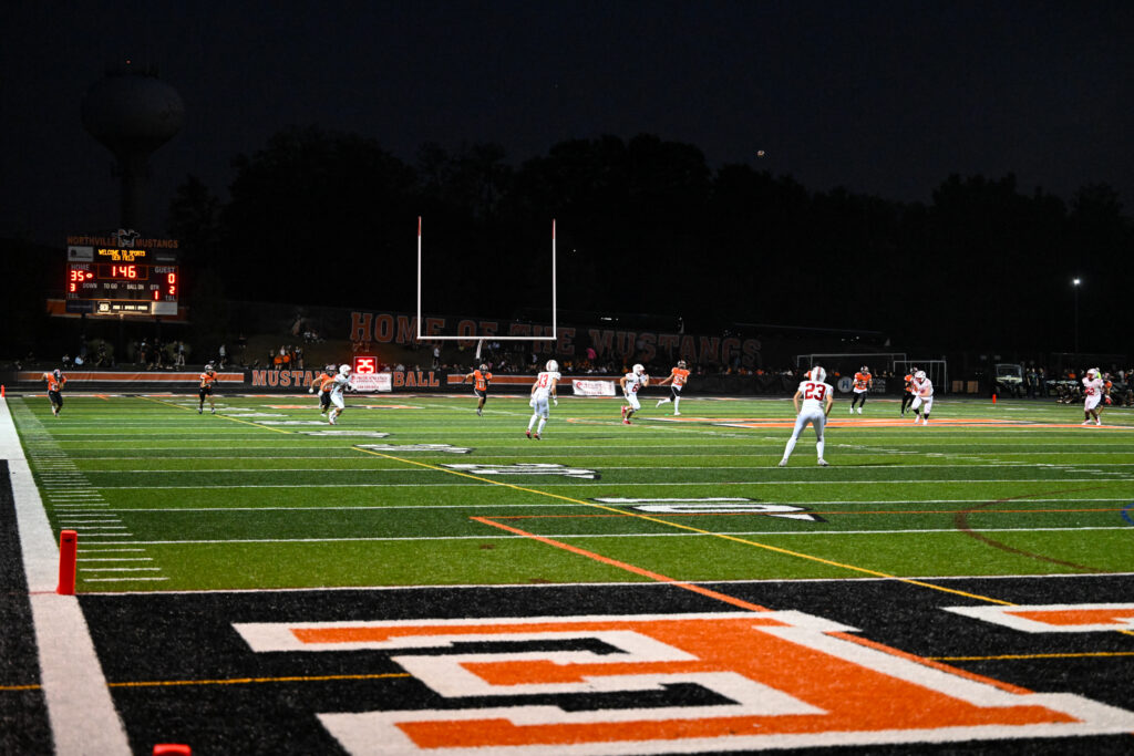 Northville Mustangs football action under the lights during a home game, representing the upcoming move to the OAA in 2027.