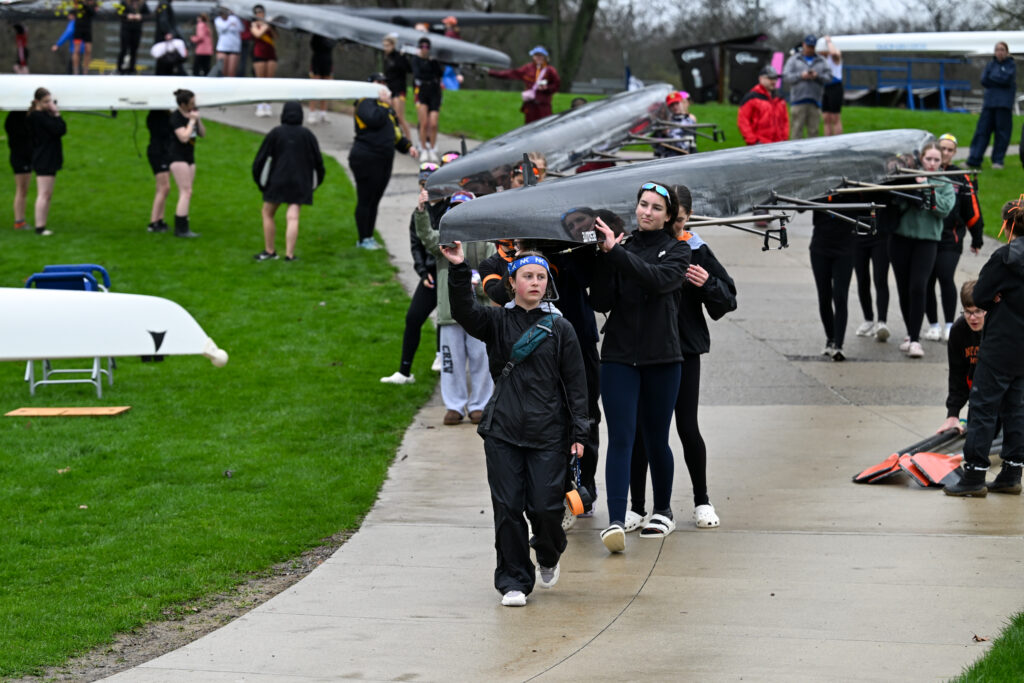 Northville Rowing carrying a racing shell to the launch dock during a spring regatta, highlighting teamwork and preparation.